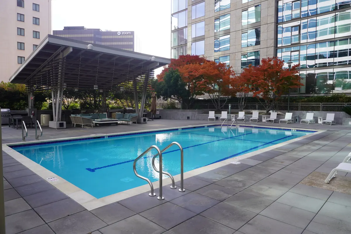 A courtyard apartment pool with chrome handrails, lounge chairs and a modern building behind it.