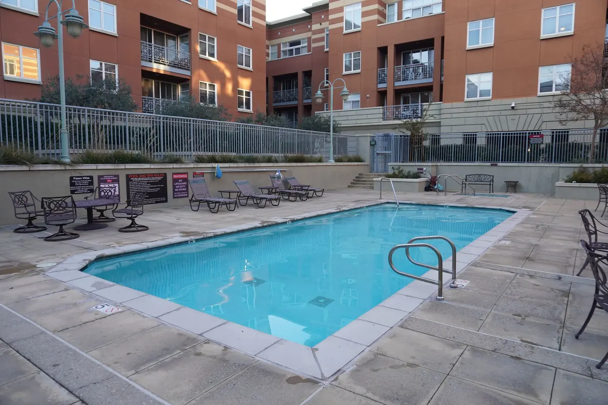 An apartment community pool with lounge chairs and a brick building behind.